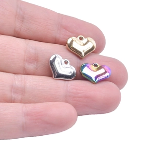 Detailed comparison of gold, silver, and rainbow heart pendants held between fingers