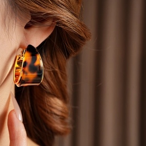 Detail of tortoise shell resin hoop earring with gold-plated lining worn by model