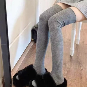 Detail of grey ribbed knit over-knee socks worn with black slippers on wood floor