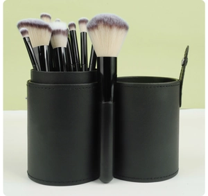 Close-up of 12 black makeup brushes with dual-tone bristles in a black PU leather cylinder case