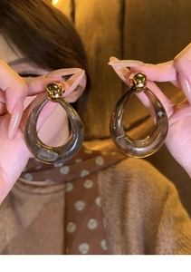 Detail of transparent brown resin teardrop earrings with gold ball studs held by a model