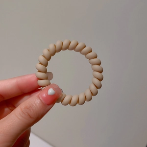 Close-up of matte beige spiral hair tie held in hand with smooth texture detail