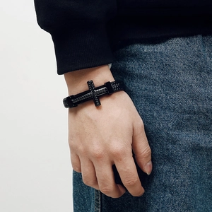 Detail of woven black leather bracelet with textured metal cross on a male wrist