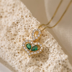 Close-up of gold heart pendant necklace with green pear-shaped gems on coral stone