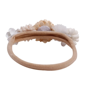 Close-up of baby headband with white and beige fabric flowers on soft nude elastic strap
