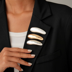 Three-piece set of sleek metallic bean brooches in gold and silver on a black blazer lapel
