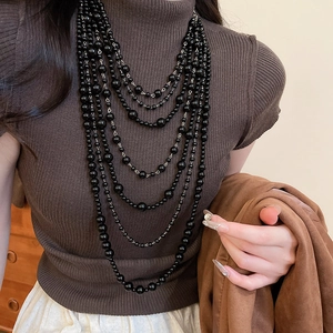 Detail view of multi-layer black acrylic beaded fringe necklace on brown sweater
