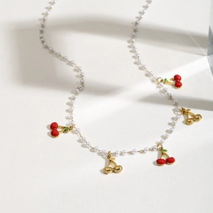 French style pearl necklace with red and gold cherry pendants on light background
