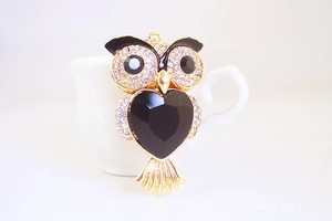 Detail of owl keychain with black heart crystal and rhinestones on a white cup