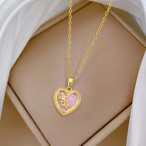 Macro detail of gold heart pendant with pink filling and floral accent on silk background