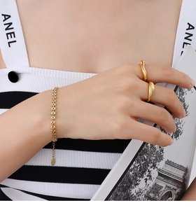 Gros plan sur un bracelet gourmette doré et des bagues gouttes fluides sur un mannequin