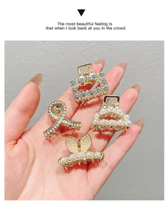 Close-up of four gold mini hair clips with pearls and rhinestones held in hand