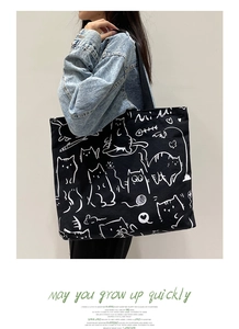 Detail of a large black canvas tote bag with hand-drawn white cat illustrations on the side