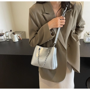 Close-up of stylish silver bucket bag with chain details worn by a model in a cafe