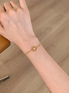 Gros plan d'un bracelet en chaîne dorée avec fleur évidée et perle centrale élégante