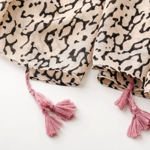 Detail of light beige scarf with black abstract print and pink braided tassels