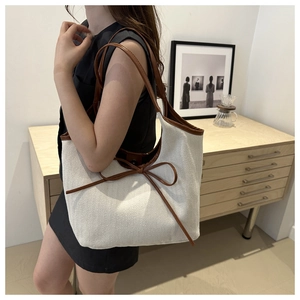 Detail of off-white canvas tote with brown leather trim worn by a model in a minimalist room