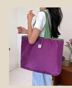 Detail of a large purple nylon tote bag with green straps and white label shown on shoulder