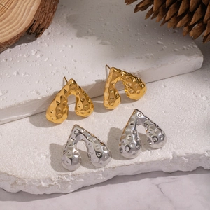 Gehämmerte Herzbogen-Ohrringe in Gold und Silber auf dekorativem Steindisplay