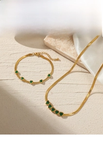 Detail of gold snake chain set with emerald heart charms on marble and silk