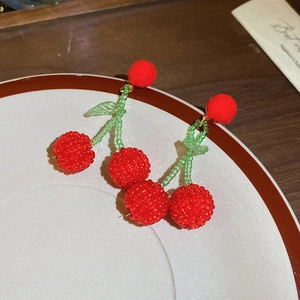 Detail of beaded cherry earrings with red plush pom-poms and green leaf accents