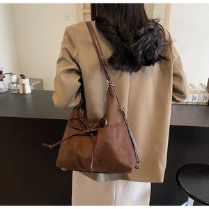 Detail of dark brown suede shoulder bag with a decorative bow knot on a khaki blazer
