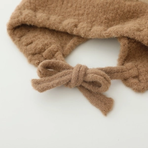 Détail du bonnet en peluche pour bébé montrant la texture douce et le nœud décoratif