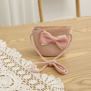 Detailed view of pink woven straw crossbody bag with white polka dot bow and lace trim