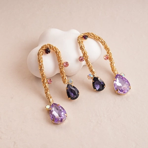 Detailed shot of gold woven teardrop earrings with purple and pink gemstone accents