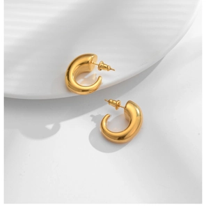 Close-up of chunky gold C-shaped earrings on a white tray with elegant soft shadows