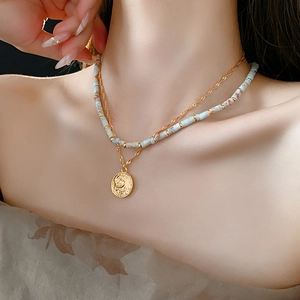 Detail view of layered gold chain with coin pendant and turquoise beaded necklace on model