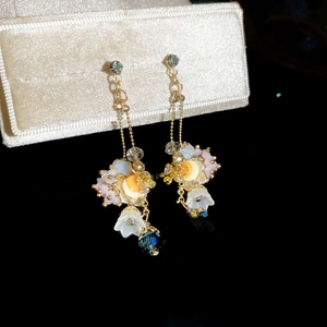 Detailed close-up of golden floral earrings with colorful beads in a luxury beige box