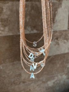 Detail of multilayer beaded necklaces with white shell initial letter pendants in champagne tone