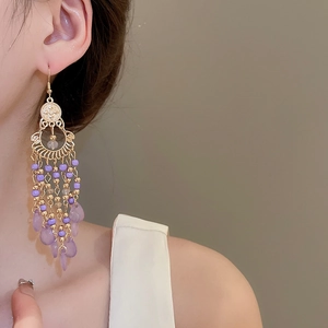 Detail of bohemian gold earrings with purple beads and teardrop tassels on model