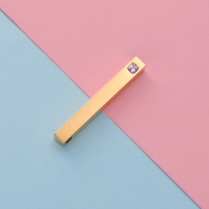 Detailed view of a gold rectangular bar pendant with an inlaid pink square gemstone