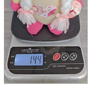 Detailed view of a pink gnome plush weight measurement 144g on a kitchen scale
