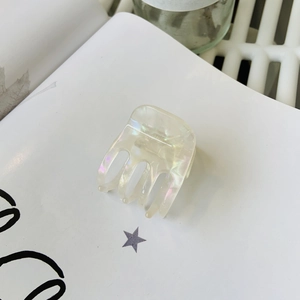 Pince à cheveux minimaliste en acétate blanc irisé sur fond de livre épuré et blanc