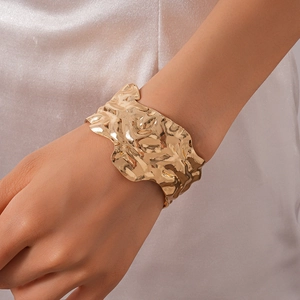 Gros plan d'un large bracelet doré avec une texture martelée irrégulière et un fini brillant