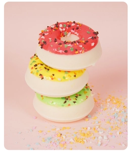 Pile verticale de trois boules de bain en forme de donut colorés sur fond rose doux