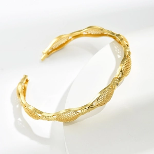 Detailed close-up of hollow woven gold geometric cuff bracelet on a white platform