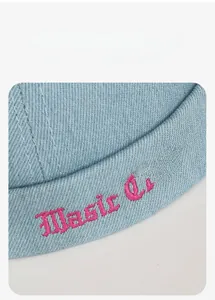 Macro detail of Music Club pink embroidery on light blue denim brimless docker cap