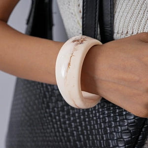 Detail shot of a thick off-white acrylic bangle with brown marble patterns on a model's wrist