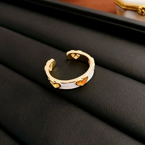 Macro detail of gold ring with orange heart charms and white enamel accents