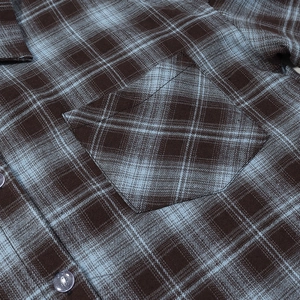 Detail of brown and blue plaid shirt featuring a chest pocket and transparent buttons