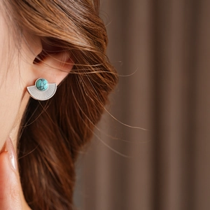Close-up of vintage fan-shaped silver earring with turquoise stone worn by model