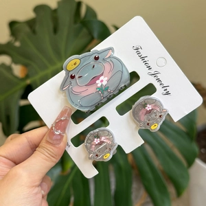 Close-up of three cute gray hippo hair clips with flowers on white display card