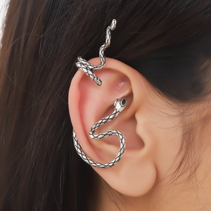 Minimalist silver snake ear cuff featuring green gem eyes worn by a model in a close-up
