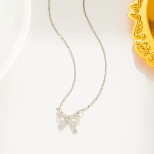 Elegant silver bow pendant necklace with sparkling diamonds on a golden jewelry tray