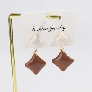 Detail of rhombic drop earrings in cream and brown enamel with gold-tone metal studs