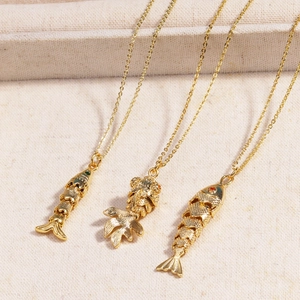 Detail of three vintage style fish pendants in gold plating with colorful gemstone eyes